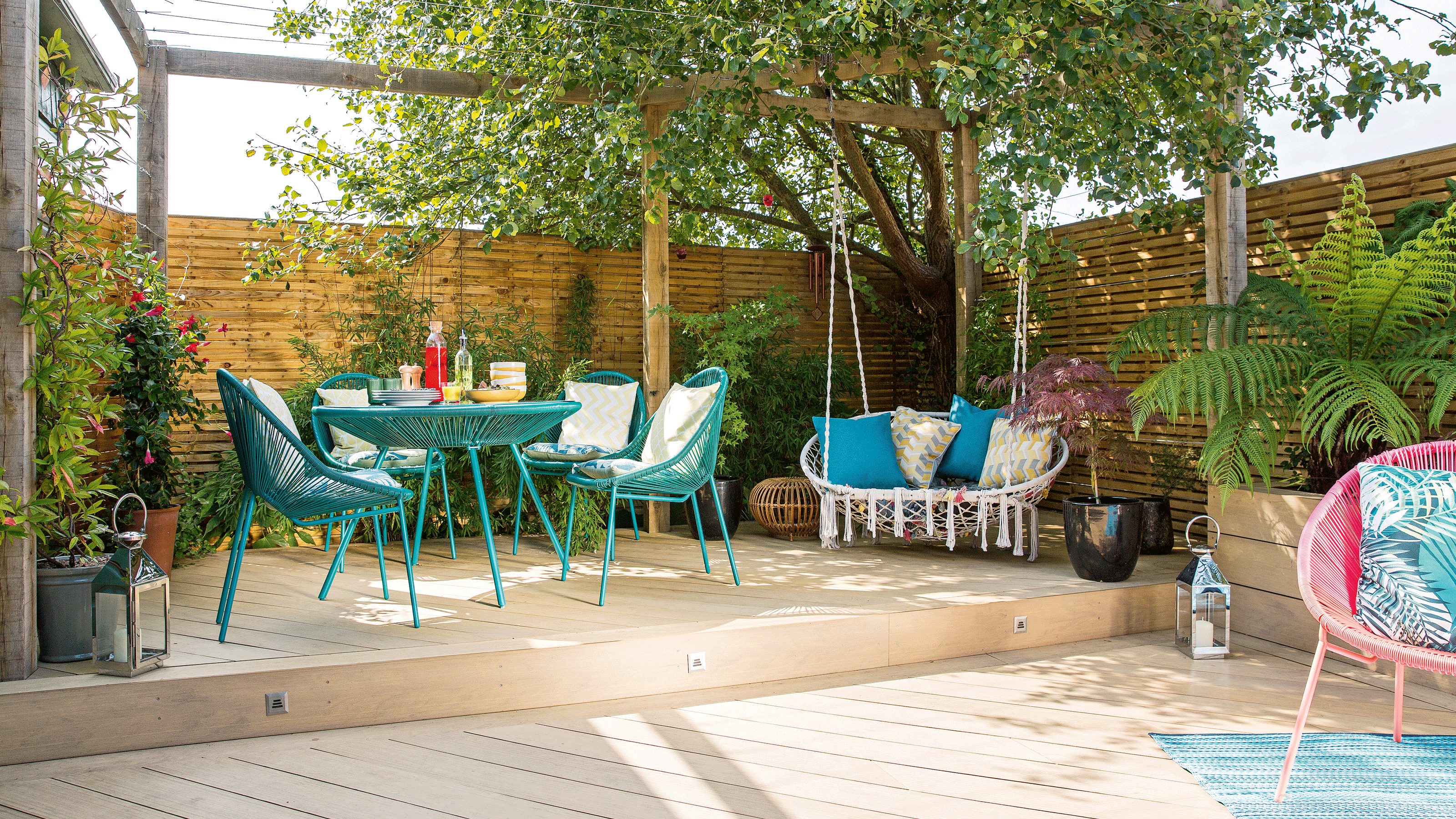 patio cover ideas, split level decking with bright furniture, hanging garden seat in corner under tree 