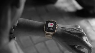 A mostly black-and-white photo of a person wearing the Apple Watch Ultra 3 — with a gold case — with a "Possible Hypertension" pop-up shown in full color.