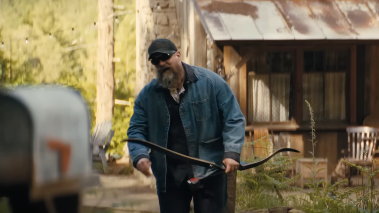 David Harbor walks towards the camera while holding a bow and arrow in A Working Man.