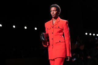 A model wears a bright red Ferragamo jacket while walking down the runway