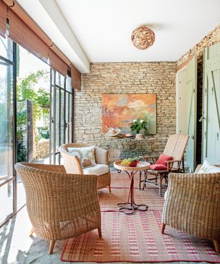living room with exposed stone wall, orange artwork, woven chairs and table, woven blinds and red woven rugs
