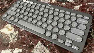 The Logitech Pebble Keys 2 K380S keyboard on a marble worktop, seen from the right-hand side.