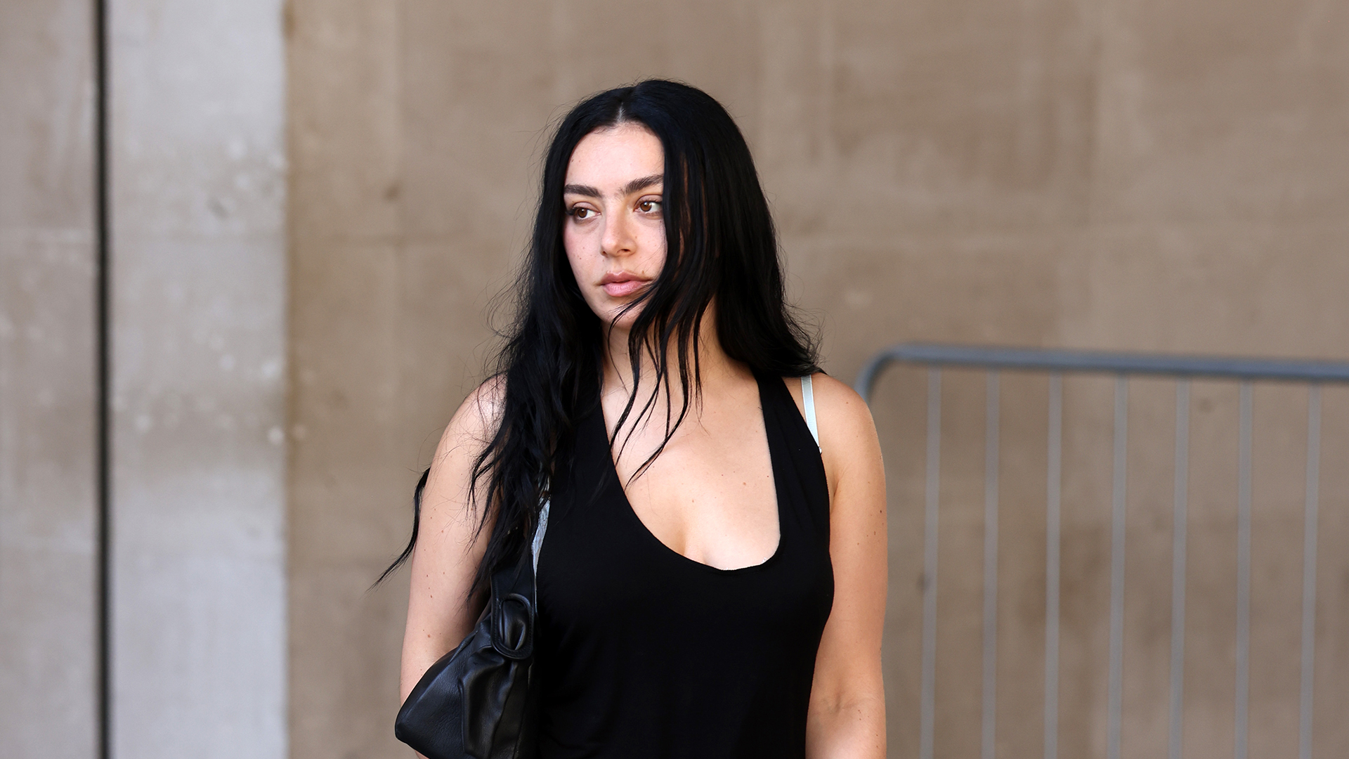 Charli xcx wearing a black mini dress, pink pumps, and a black bag