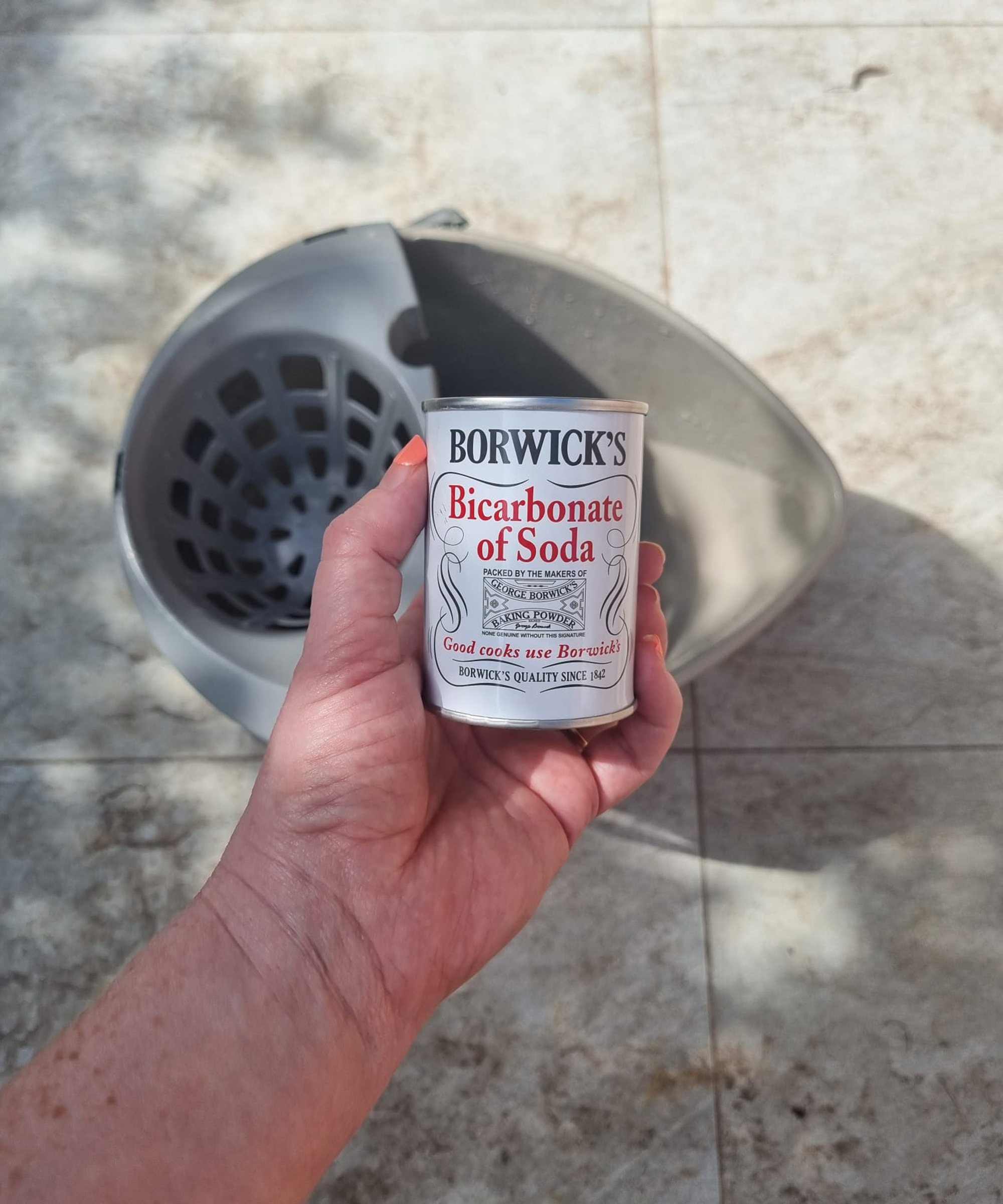 Hand holding a small tin of bicarbonate of soda ready to pour into a bucket