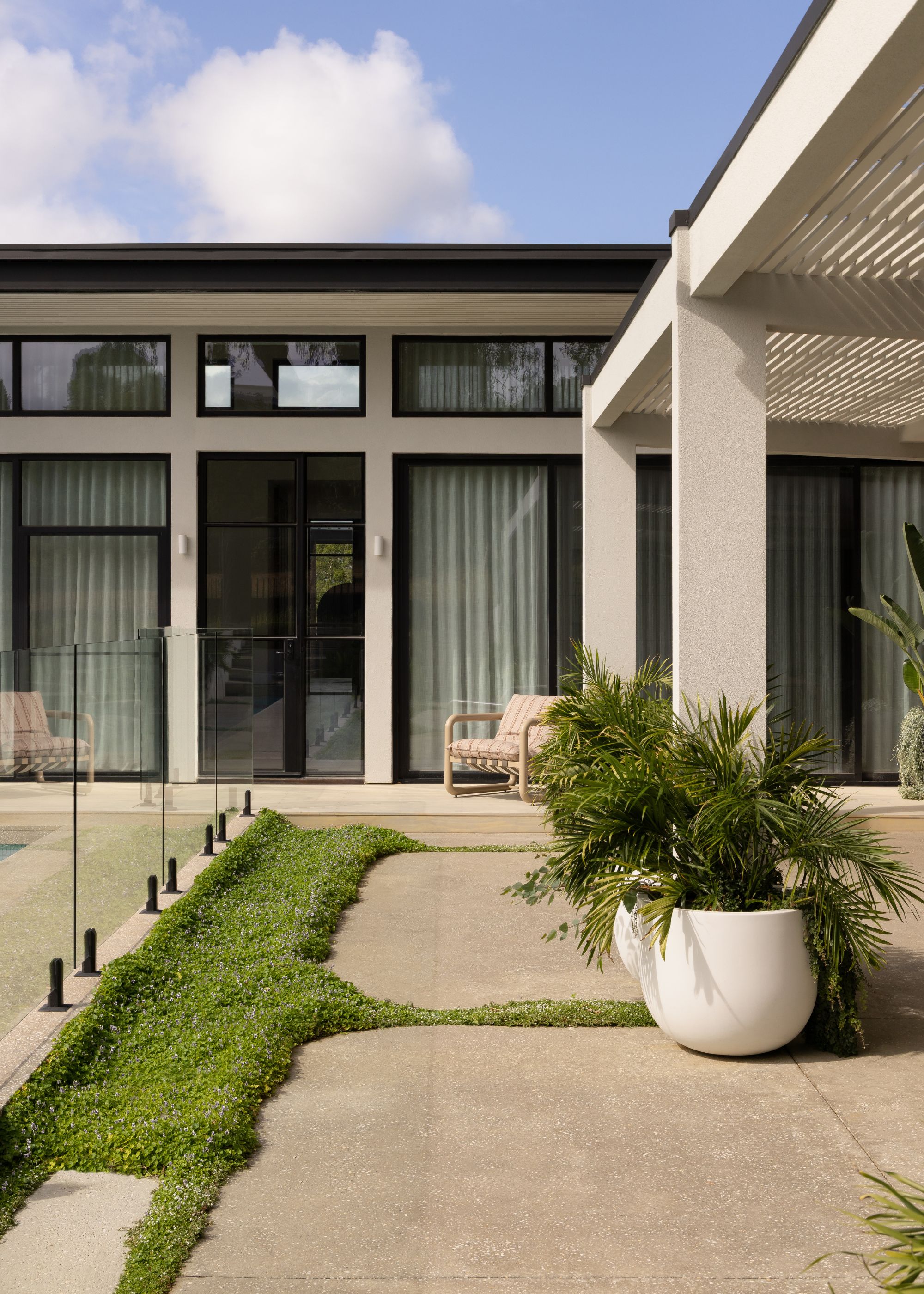 A garden with a pool, ground cover, potted palms, and a striped garden chair