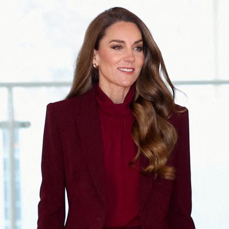 Kate Middleton walks next to Prince William wearing a burgundy suit with a brown bag and shoes.