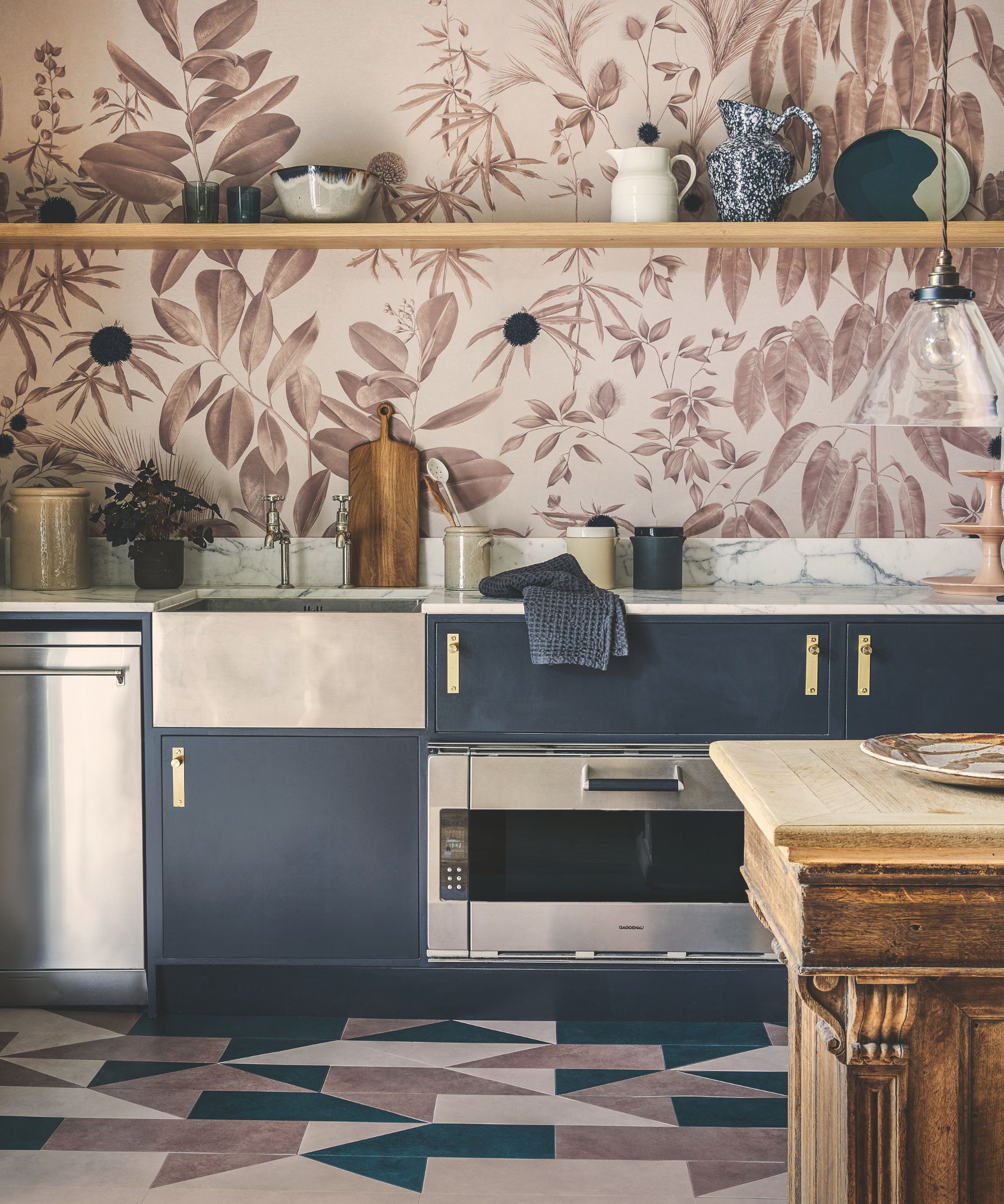 A kitchen with statement wallpaper, open shelving, geometric flooring, blue cabinets and a stainless steel sink.