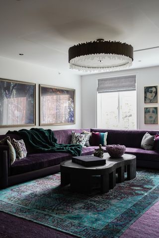 A living room with purple sofa, purple carpet and a green overlaid carpet