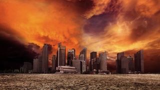 A cloudy burning orange sky hangs above a desert wasteland with the towering ruins of a modern city decaying on the horizon. 