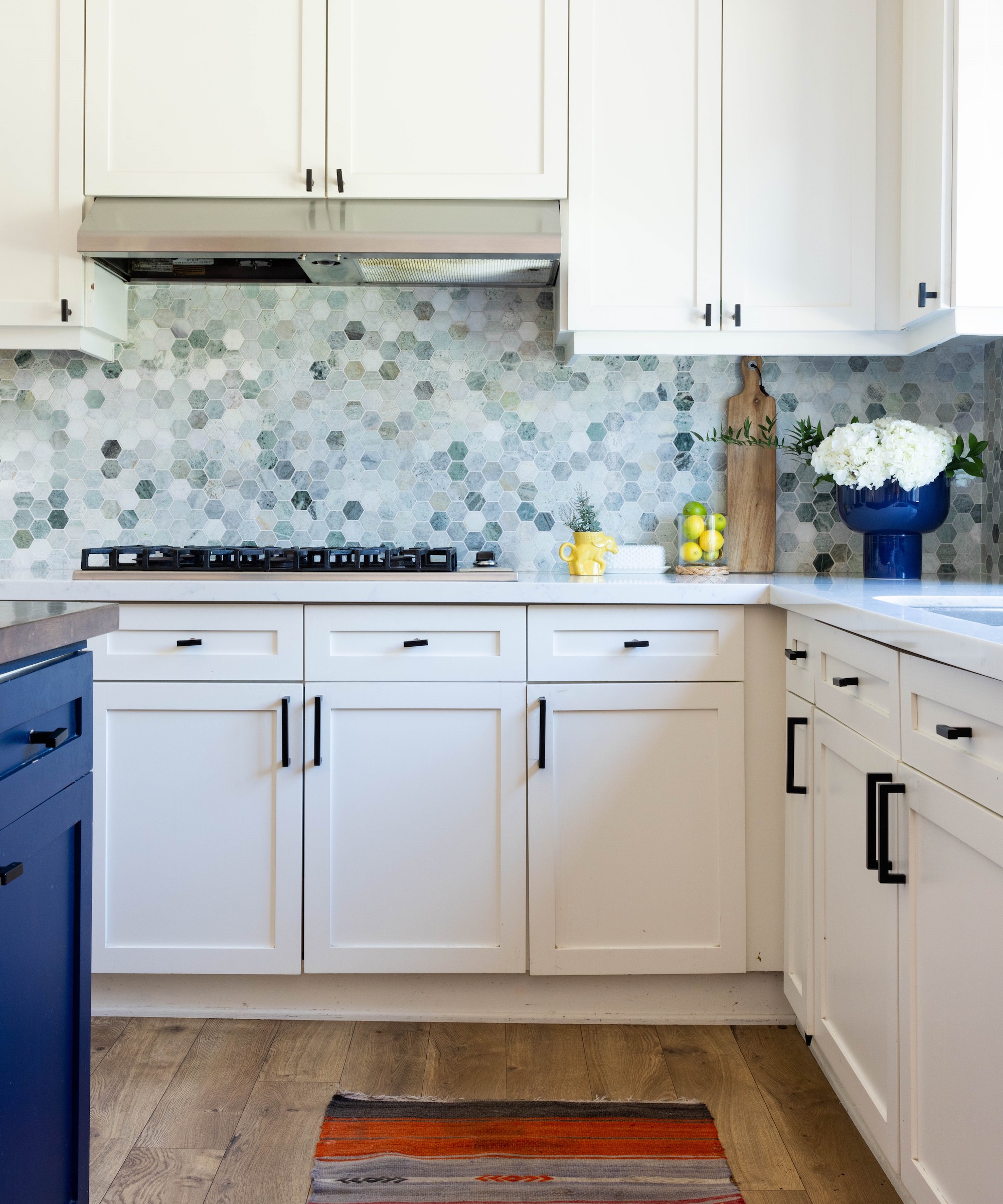 Kitchen with warm white cabinets, blue island, light countertop and blue hexagonal pattern backsplash