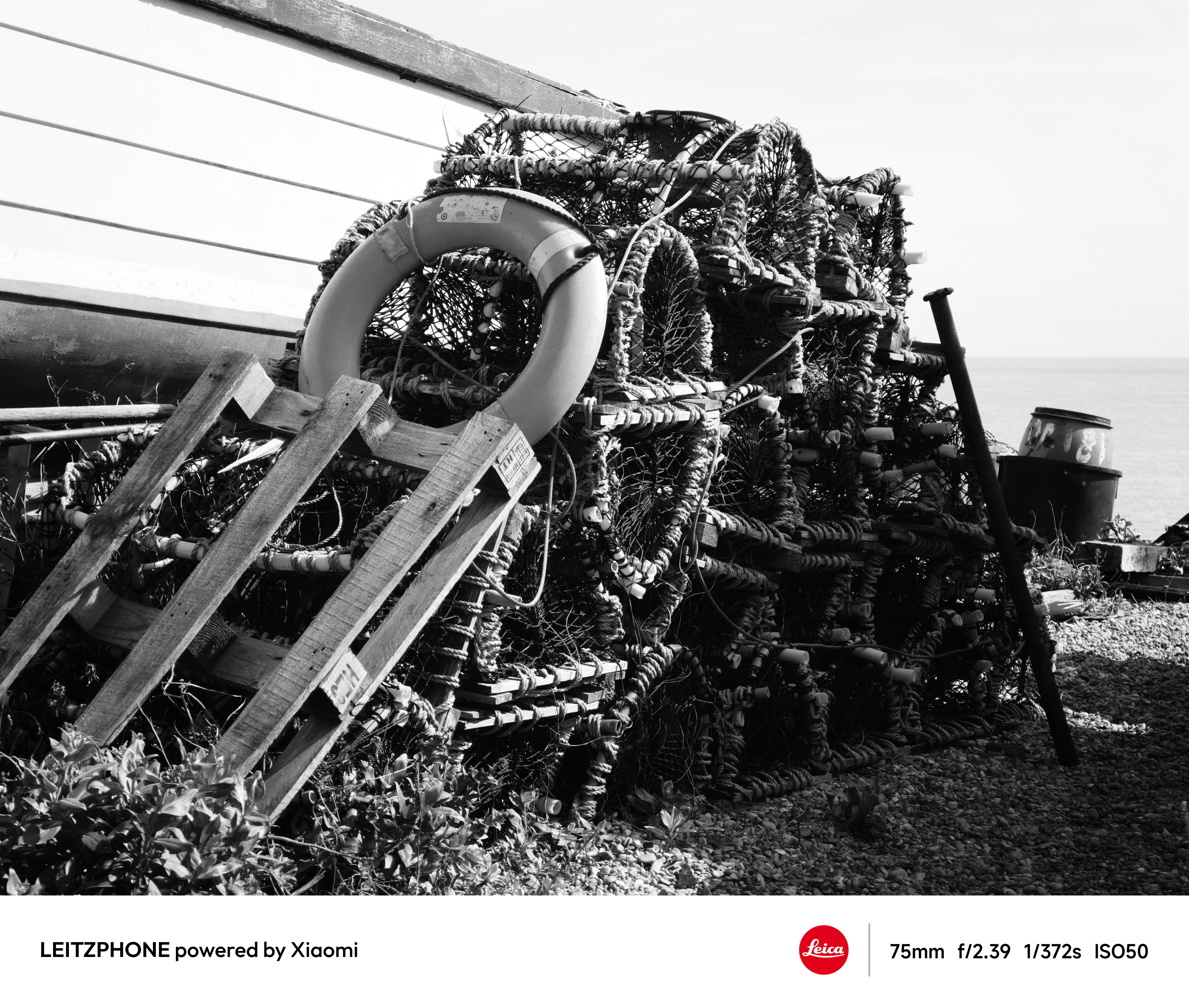Black-and-white photo of stacked lobster pots and a lifebuoy