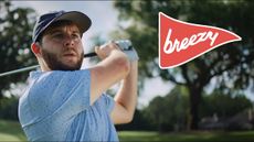A golfer wearing Breezy Golf apparel takes a swing