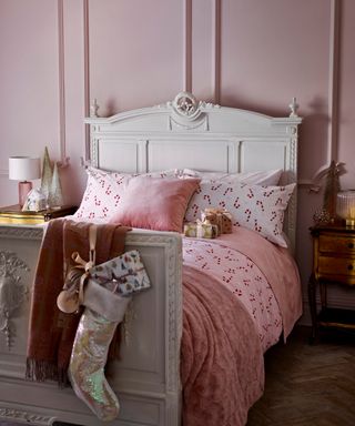 A pink Christmas-themed bedroom with candy cane bedding and white bed frame with ornate detail
