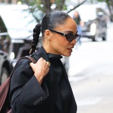 Tessa Thompson wearing a black coat, a plisse top and skirt, brown loafers