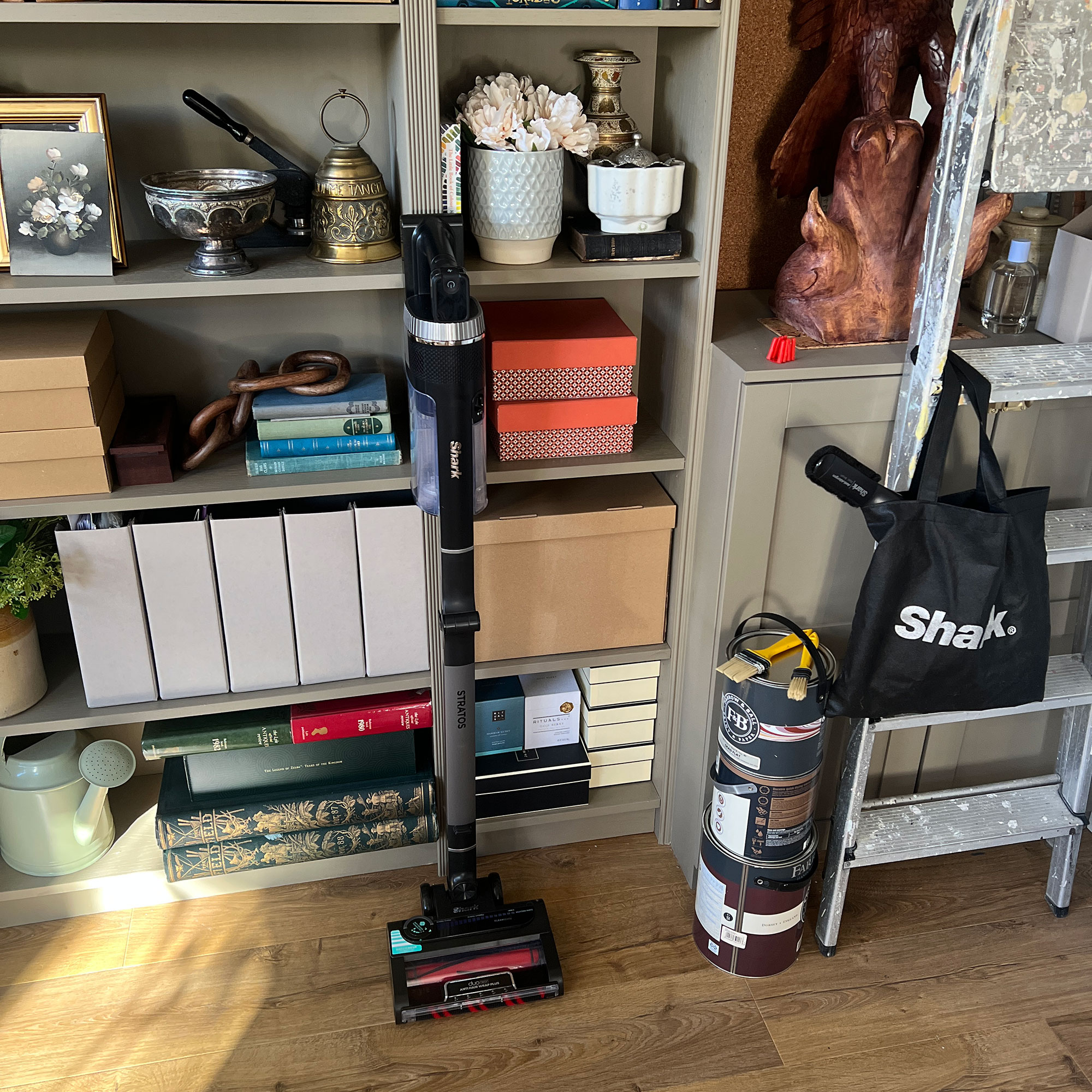 Shark cordless vacuum leaning against green-grey bookcase