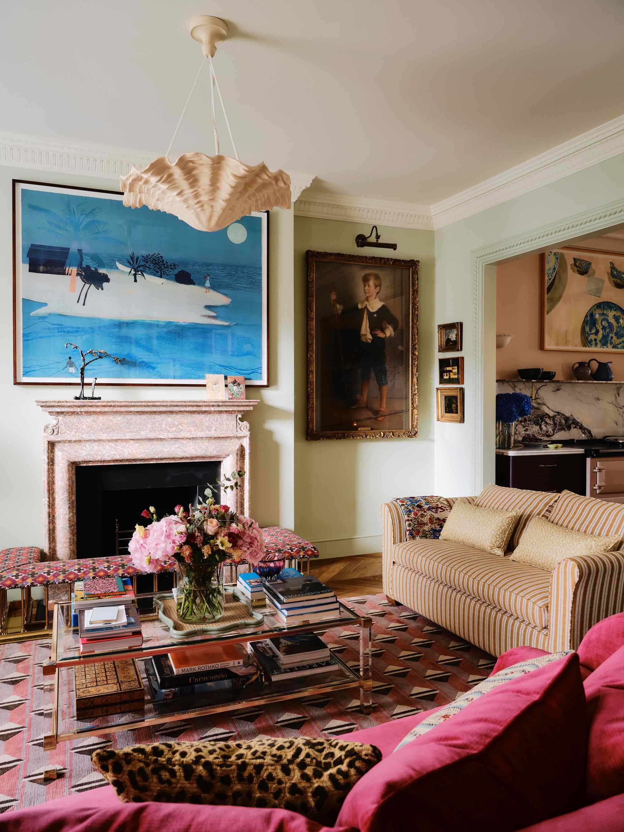 Image of a light green living room with art on the walls, a pink marble fireplace, a striped sofa, a geometric rug, and a red sofa with a cheetah print pillow.