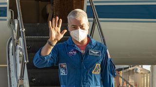 astronaut mark vande de hei leaving airplane via stairs, waving and wearing a mask
