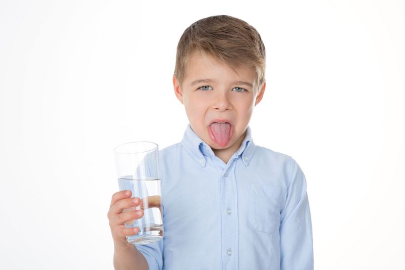 A little boy holds up a glass of water that tastes bad.