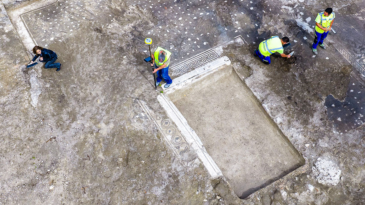 archaeologists work at an ancient Roman site revealing mosaic floors and frescoed walls of a villa