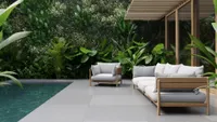 A Japanese-style garden with a wooden outdoor sofa and armchair upholstered with grey cushions
