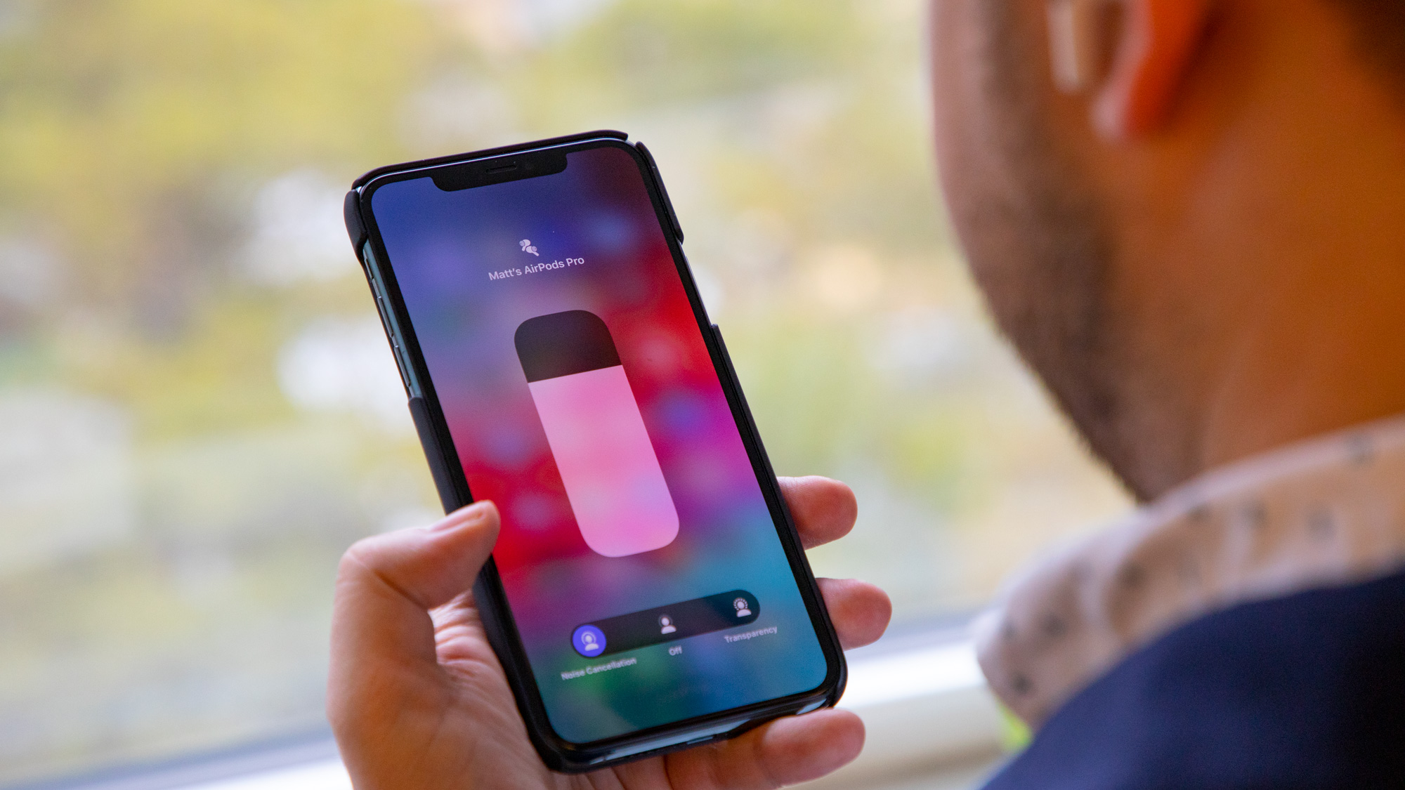 A person holding an iPhone and controlling the AirPods Pro, you can see a volume slider on the screen.