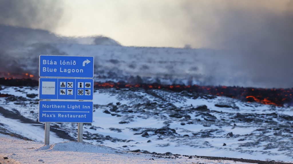 A road sign pointing to the Blue Lagoon resort and Northern Light Inn in Svartsengi stands in the foreground of a lava flow.