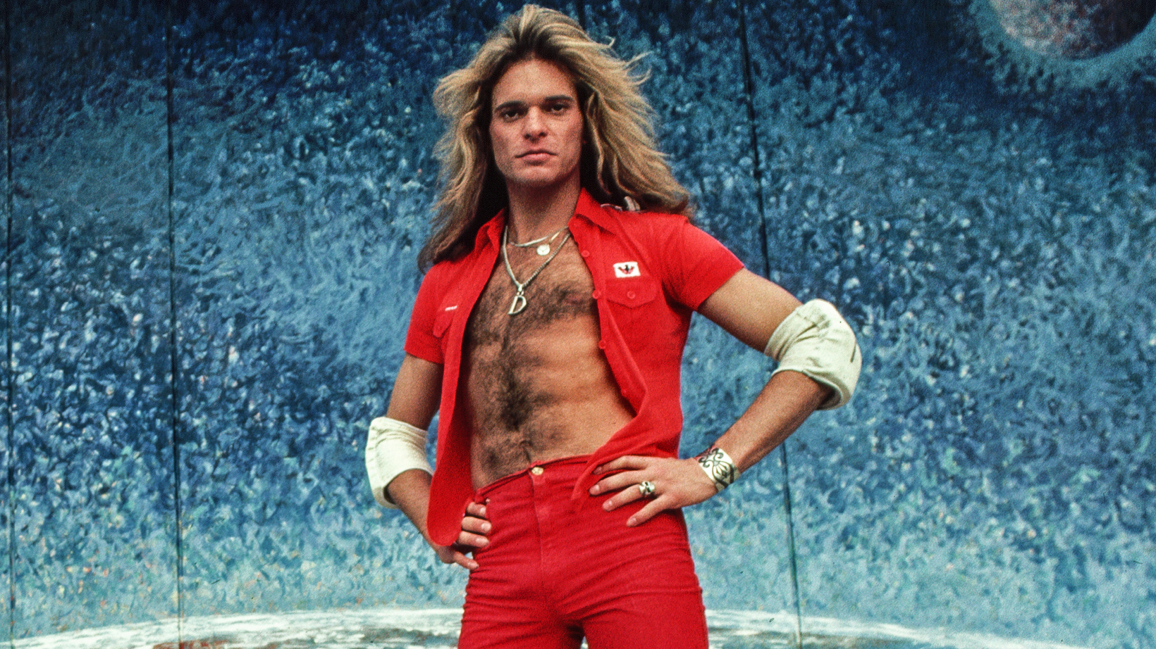 Van Halen's singer David Lee Roth rollerskates in front of a mural of Earth and the Moon. 