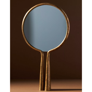 round small mirror with a brushed gold rim which elongates to two standing rods