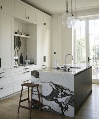 marble clad island in white kitchen with wood floors