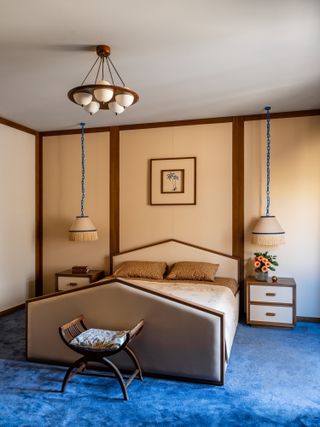 A bedroom with beige walls and bed, and dark blue carpet