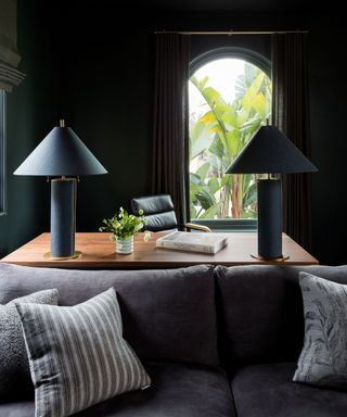 home office with dark paint and dark gray sofa and arched window