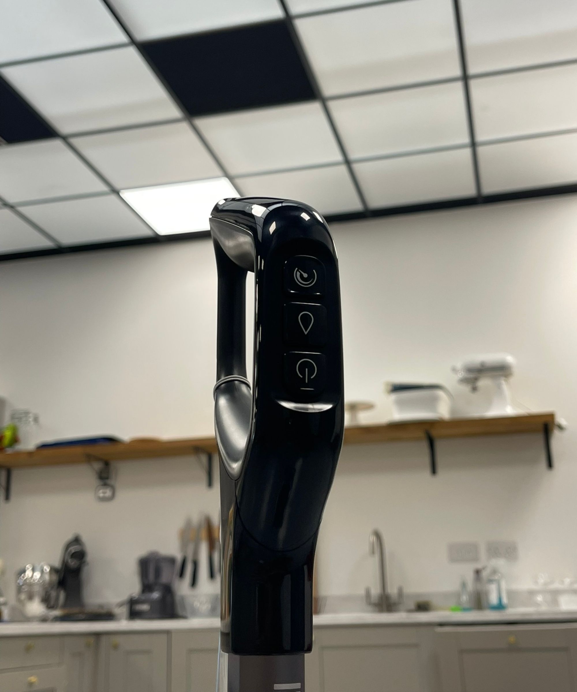 Closeup of Bissell CrossWave OmniForce Edge handle with three buttons (power, level, moisture) in Future test center with kitchen cabinets and shelf pictured in background.
