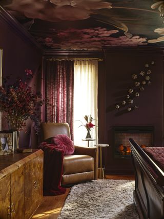 A bedroom with dark brown walls, floral wallpaper on the ceiling, and a brown leather chair in the corner