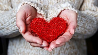 A pair of hands carefully hold a soft red crocheted heart.