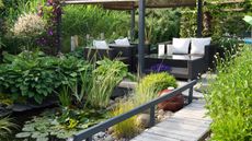A contemporary garden with water feature, hostas, pergola, and padded furniture
