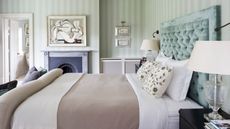 Green striped bedroom with velvet headboard, mantelpiece and abstract art
