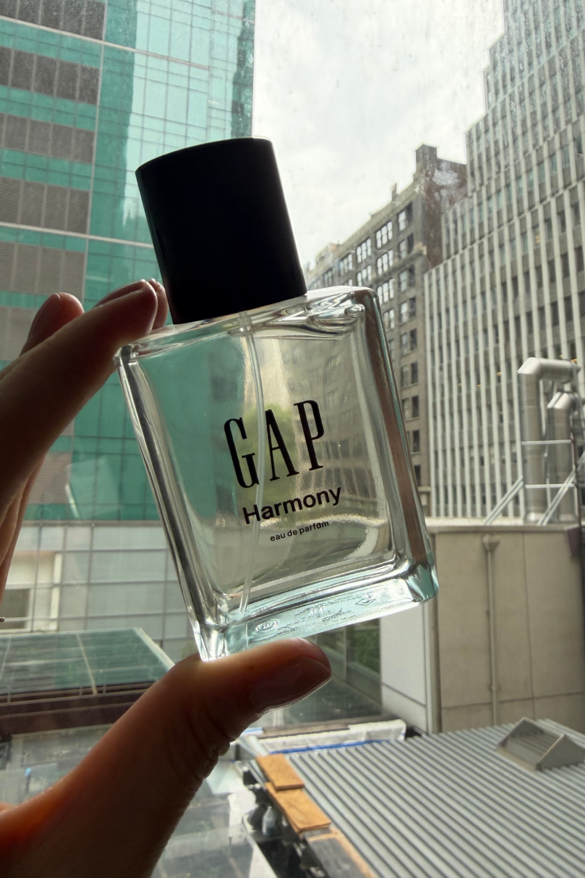 a hand holding up a glass bottle of Gap harmony perfume to a window