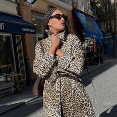 Woman wears leopard-print trench coat and black sunglasses, walking down Paris street.