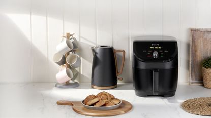 An Instant Vortex Slim air fryer on a countertop next to an electric kettle and a plate of cinnamon rolls