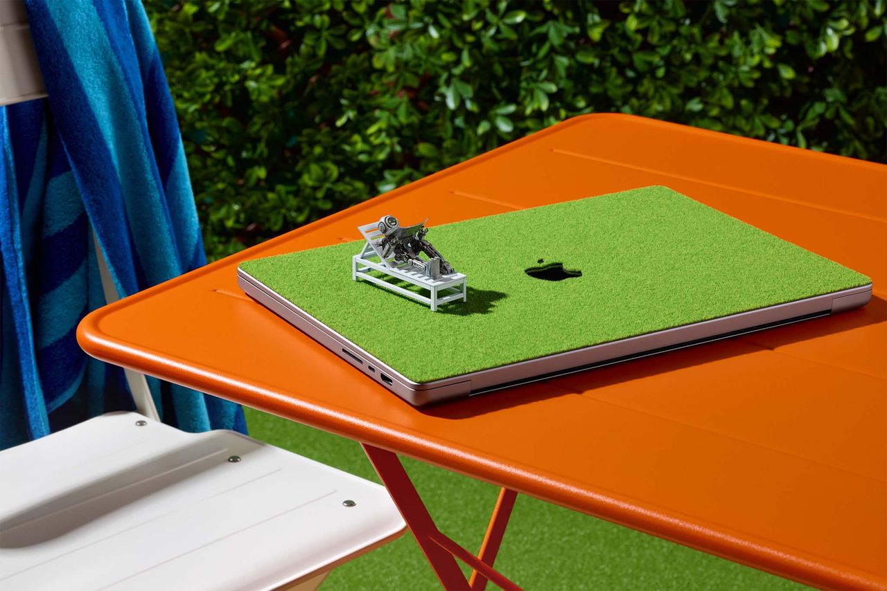 dBrand Touch Grass skin on a MacBook. The MacBook is outside on an orange table.