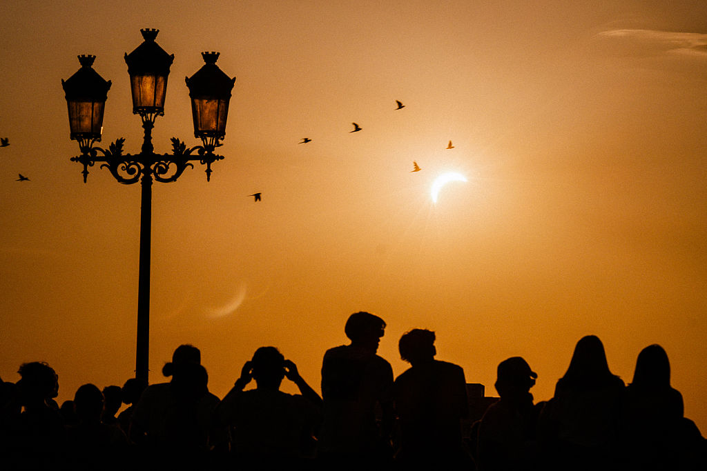 Silhouettes of people walk by or watch the partial solar eclipse (wearing protective glasses) covering nearly 98% of the sun along the banks of the Garonne River in the city of Toulouse, in southwestern France, on August 12, 2026.