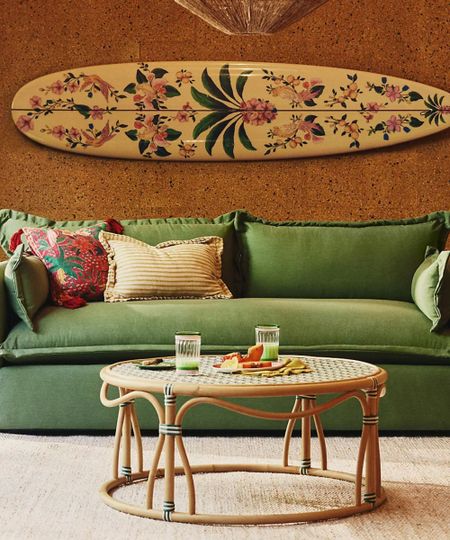 lifestyle shot of a living room with green sofa, round coffee table and floral patterned surfboard on the wall