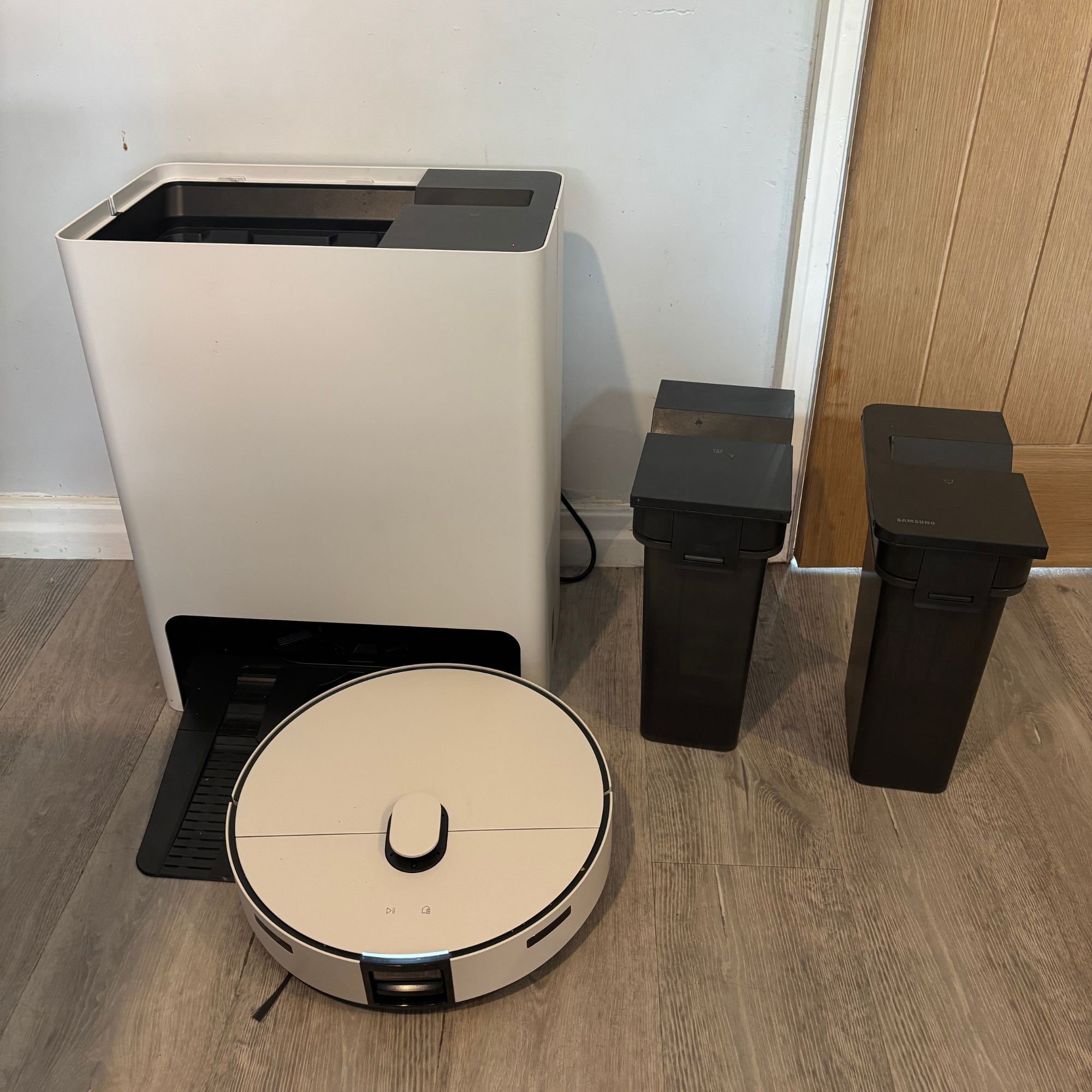 White Samsung robot vacuum with base, with clean and dirty water tanks sitting next to it