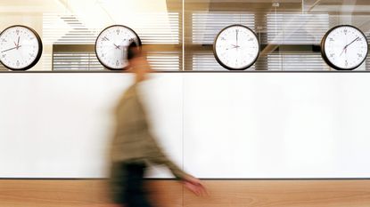 A blurry figure speeds past four clocks on an office wall.