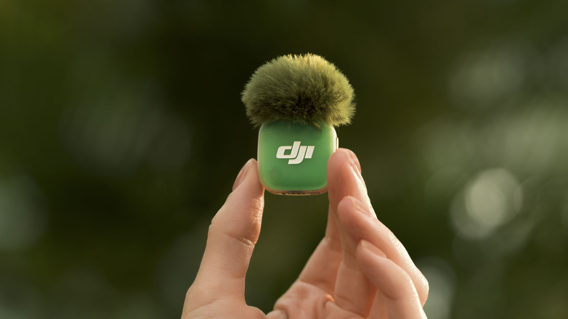 DJI Mic Mini 2 mic in green with green windshield in person's hand, with natural green background