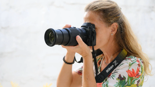 The Nikon Z 24-200mm f/4-6.3 lens attached to a Nikon camera held up to person's eye with summer ocean backdrop