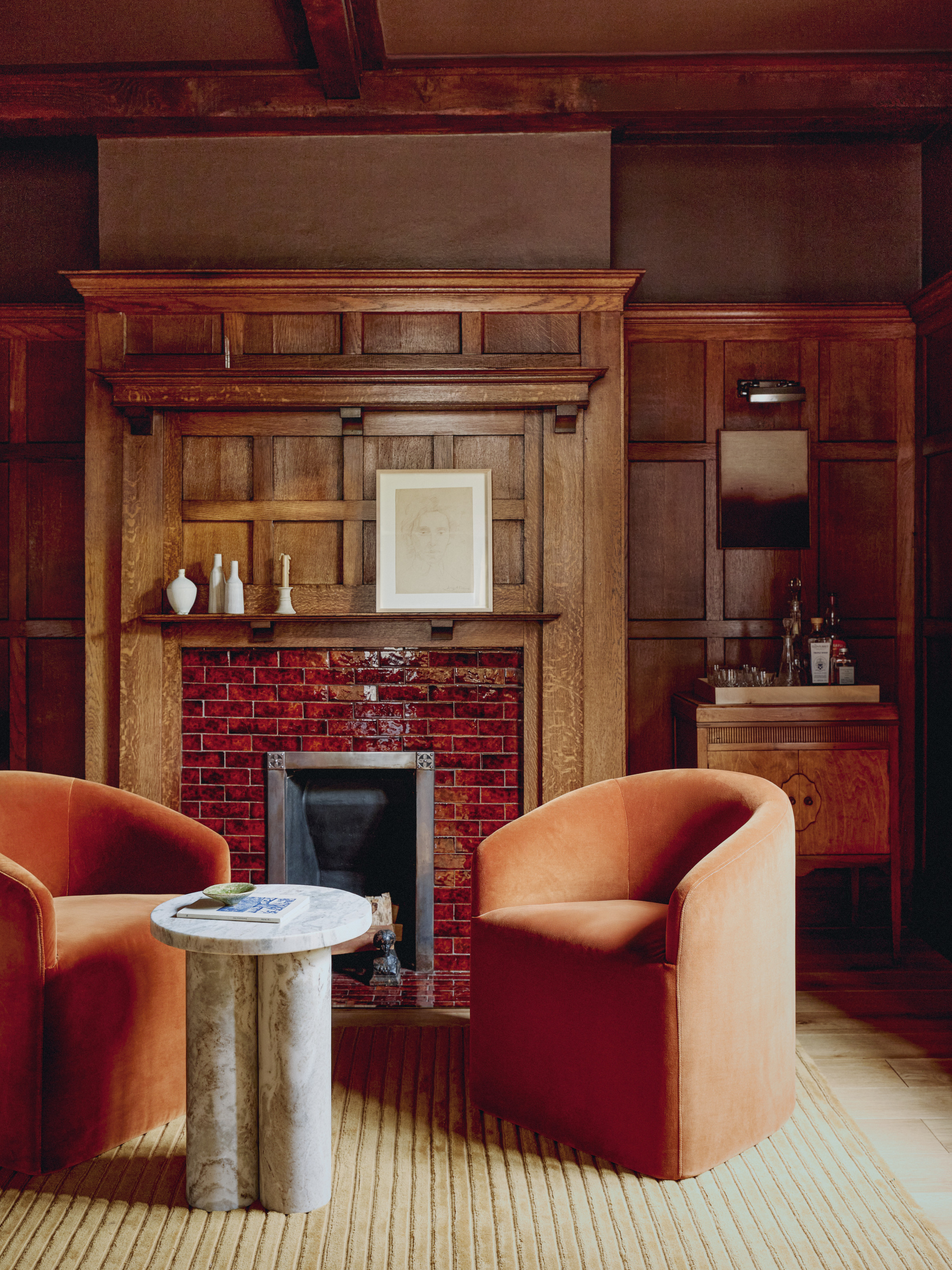 Bar seating area with oak paneled walls, orange tub armchairs, stone side table and burl wood bar cabinet