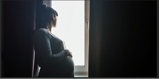 Pregnant woman looks longingly out of a window.