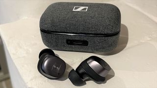 Sennheiser Momentum True Wireless 3 earbuds with charge case on a white brick surface