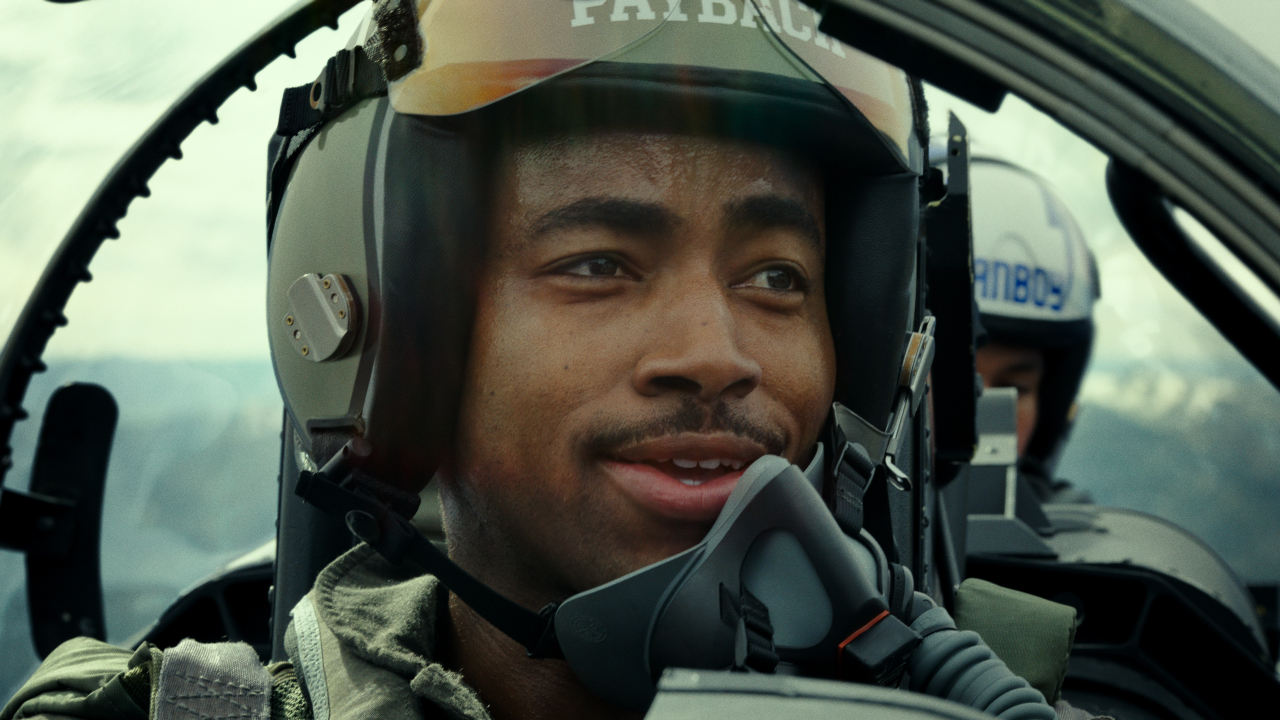 Jay Ellis smiles as he talks in his cockpit in Top Gun: Maverick.